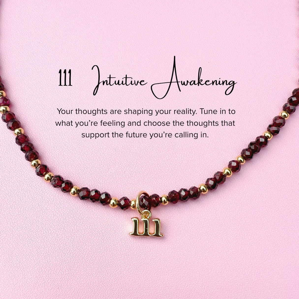 Necklace featuring maroon garnet beads and a gold 111 angel number charm on a pink background, accompanied by text about intuitive awakening.