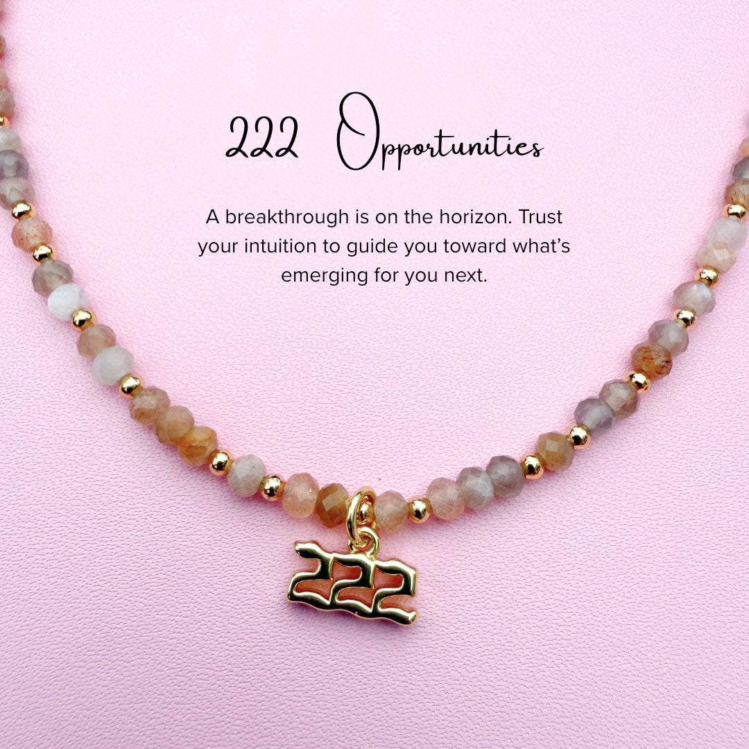 Peach moonstone beaded Necklace with gold '222' angel number charm on a pink background