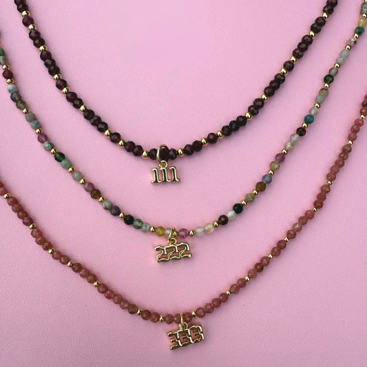 Three beaded crystal necklaces with angel number charms 111, 222, 333 on a pink background