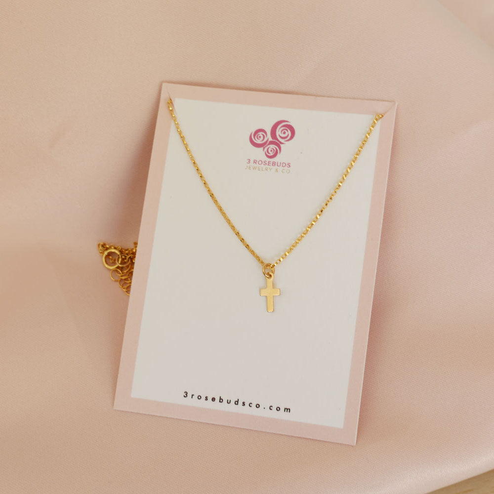 girls gold filled necklace with cross pendant on a pink background