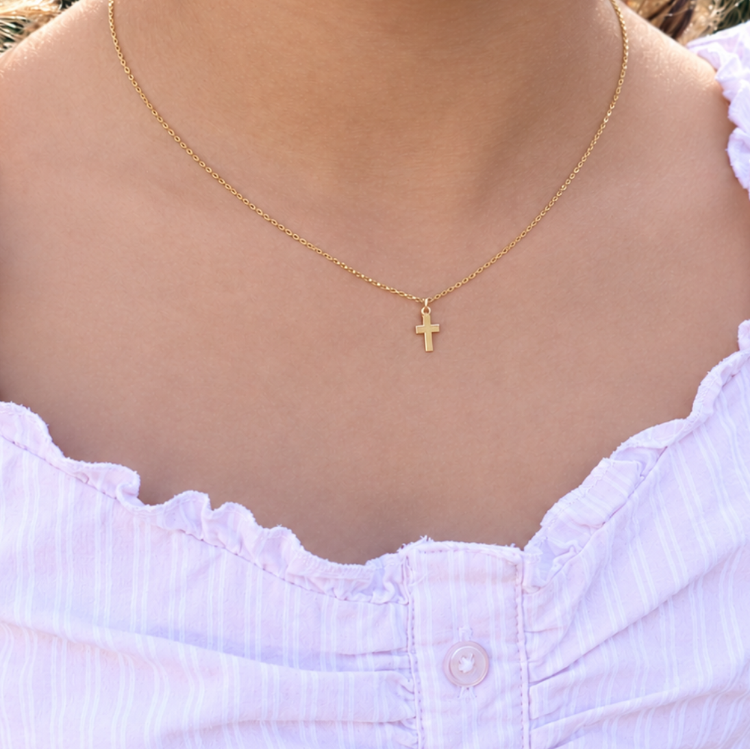 Gold cross necklace on a girl wearing a pink shirt 
