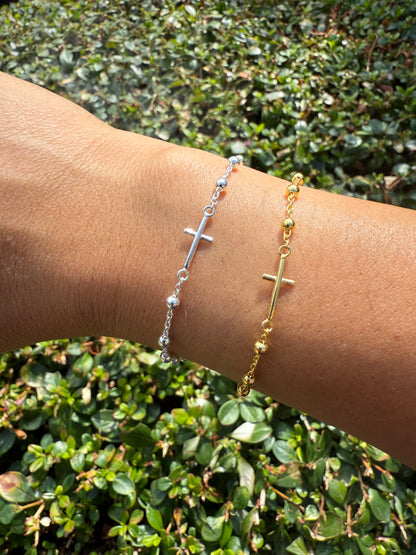 Gold and silver cross bracelets on a wrist with a green leafy background