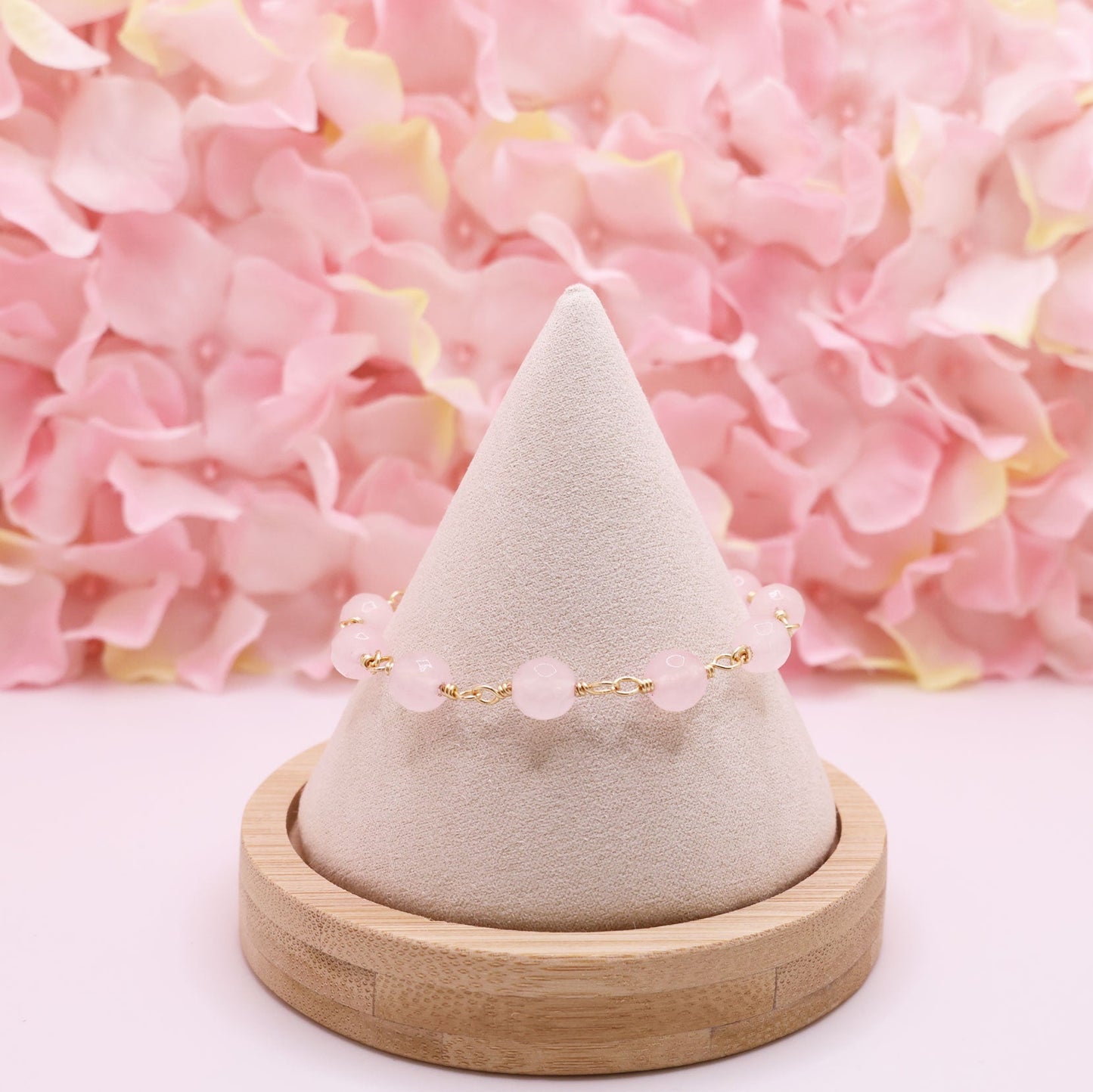 rose quartz rosary bracelet on a cone-shaped jewelry stand with pink flowers in the background