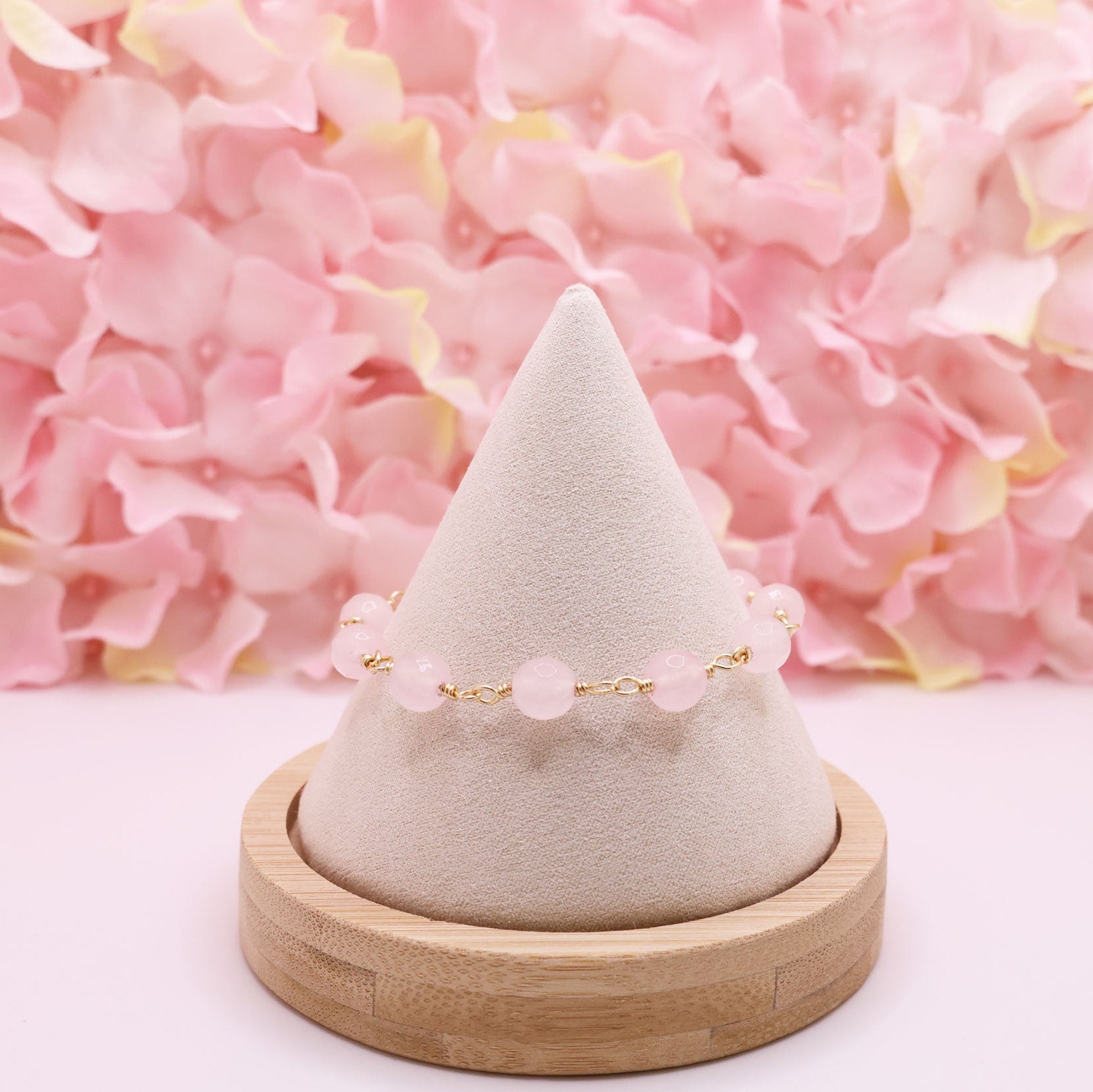 rose quartz rosary bracelet on a cone-shaped jewelry stand with pink flowers in the background