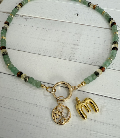 Prosperity Necklace with green crystal such as green aventurine, pyrite, citrine and tigers eye. Necklace is finished and accented with gold fittings and gold charms on a white wooden surface