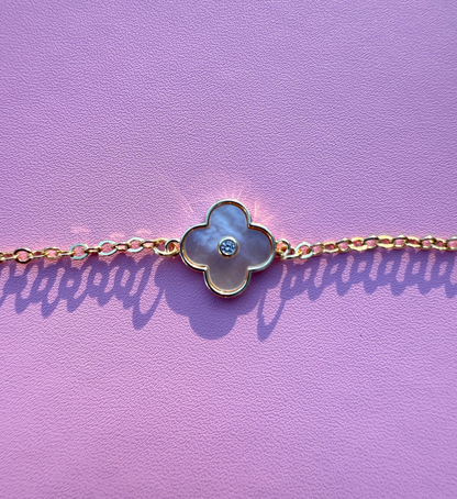 Gold bracelet with a  mother of pearl clover-shaped charm on a purple background