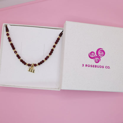 Necklace with a gold charm on a box labeled '3 Rosebuds Co.' against a pink background