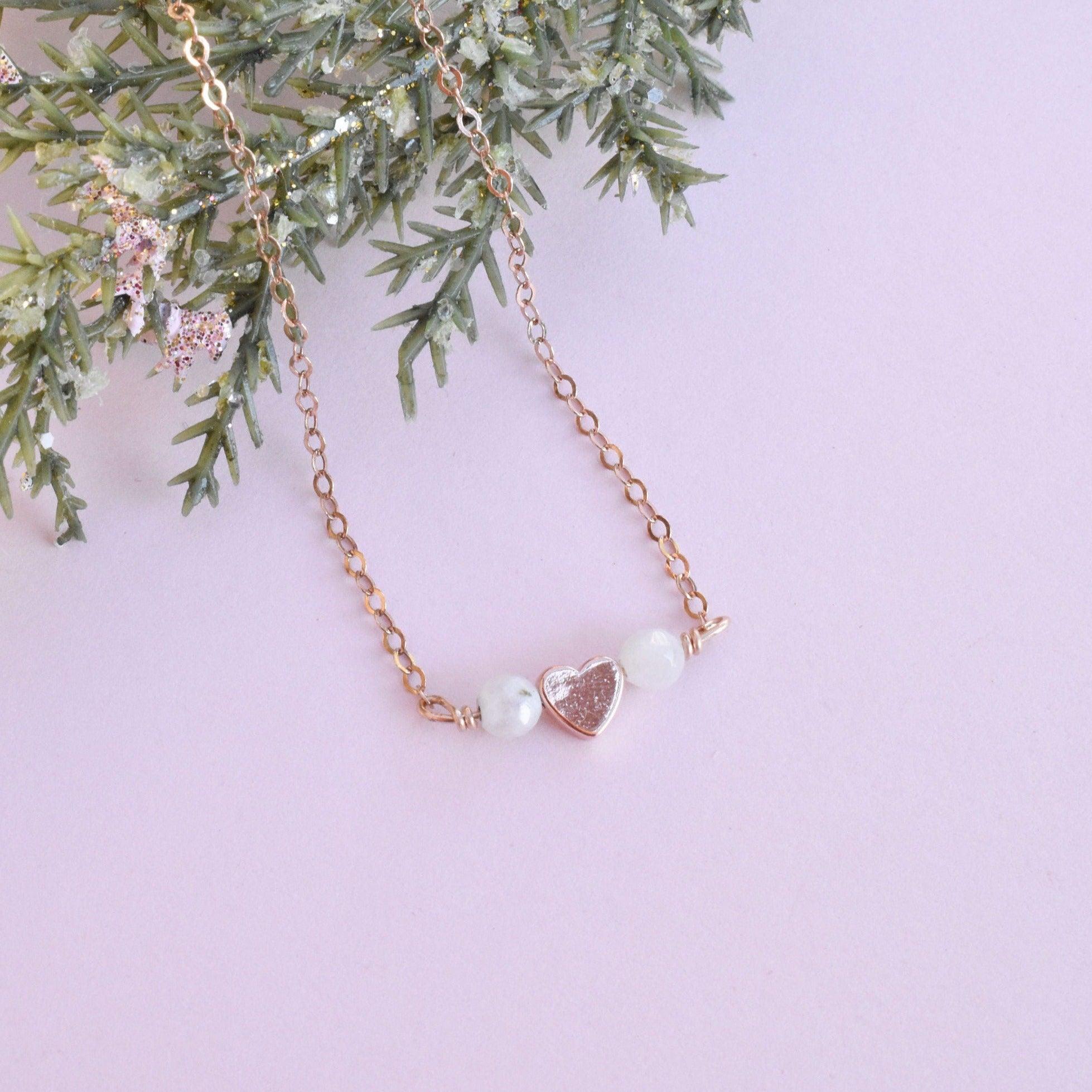 Dainty rose gold heart necklace with either rainbow moonstone or pink opal. It features a 14k rose gold-filled necklace and power stones that promote love and positivity.